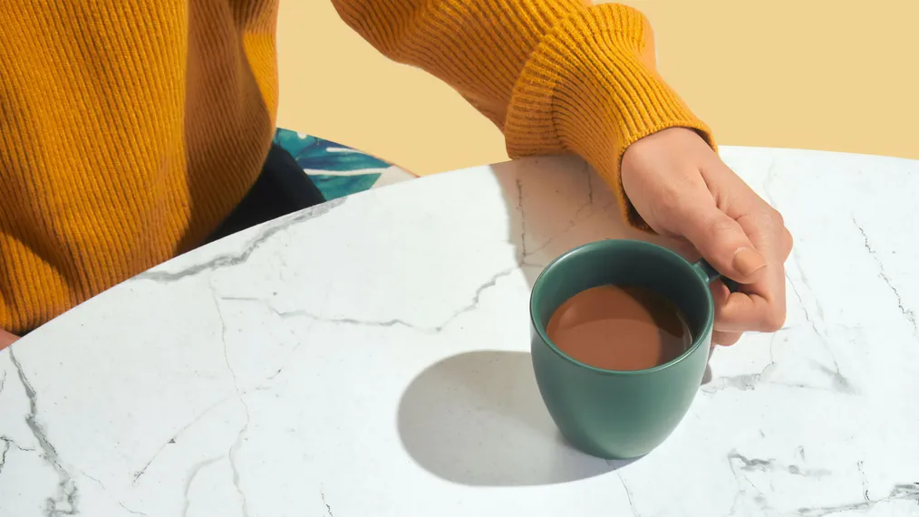 Xícara verde sobre mesa de mármore, ao lado de uma pessoa de suéter amarelo